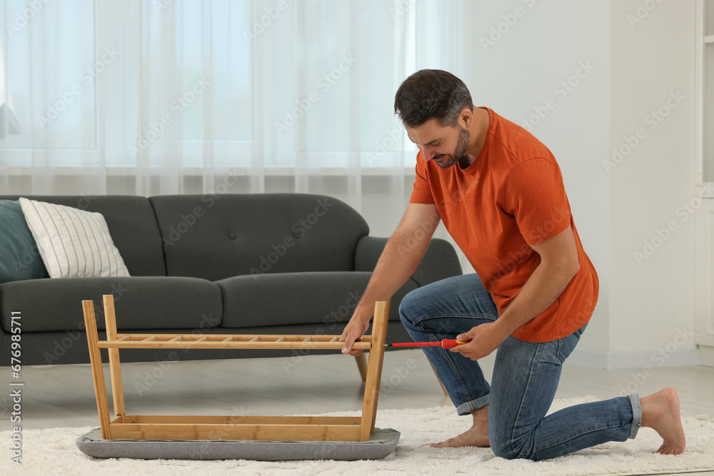 Man assembling shoe storage bench with screwdriver on floor at home