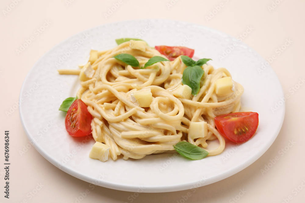 Delicious pasta with brie cheese, tomatoes and basil leaves on beige table, closeup