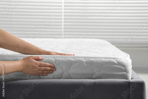 Woman touching soft light green mattress indoors, closeup