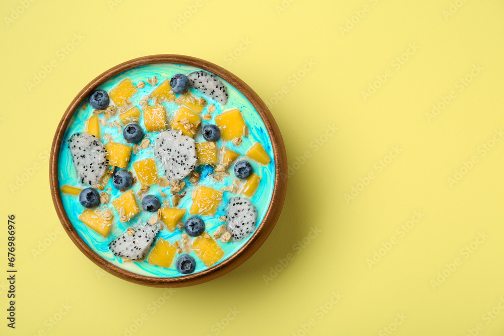 Delicious smoothie bowl with fresh fruits, blueberries and oatmeal on yellow background, top view. Space for text