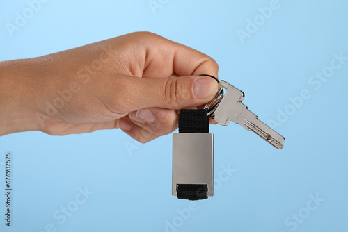 Woman holding key with keychain on light blue background, closeup