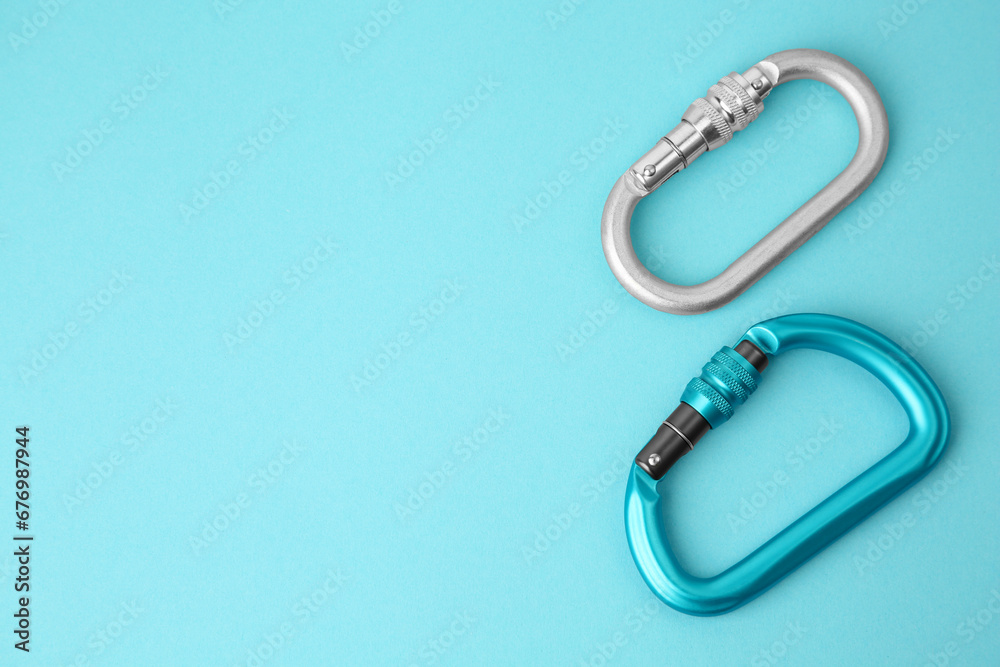 Fototapeta premium Two metal carabiners on light blue background, flat lay. Space for text