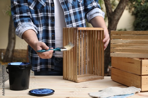 Man applying varnish onto wooden crate at table outdoors, closeup photo