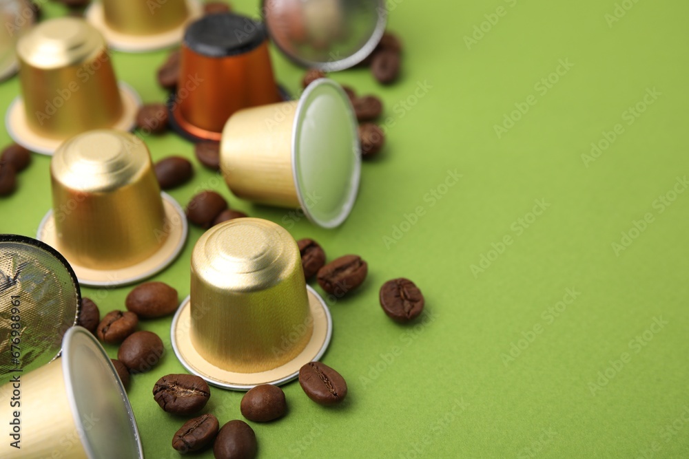 Many coffee capsules and beans on green background, closeup. Space for text