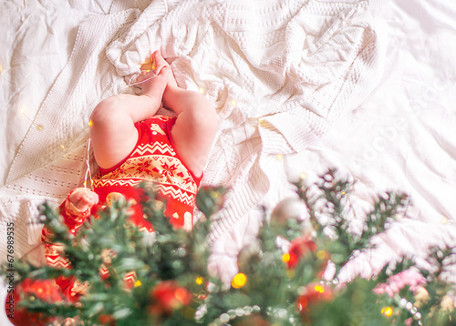 Newborn baby in red clothes located under the decorated christmas tree.
