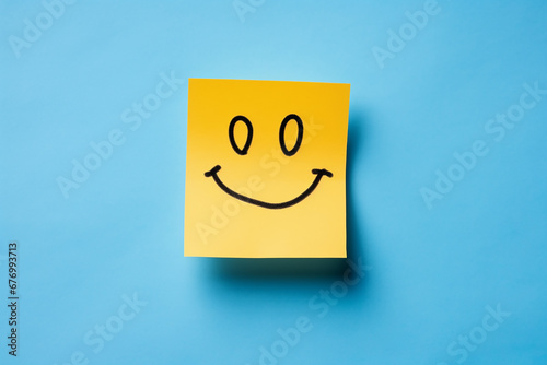 Positive attitude concept, happy hand drawn yellow color sticky note, smiling sticky note paper isolated in blue background.