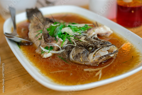 steam fried Marbled Goby fish called Ikan Malas in siamese style served in a dish on a wooden table in a restaurant in Indonesia photo