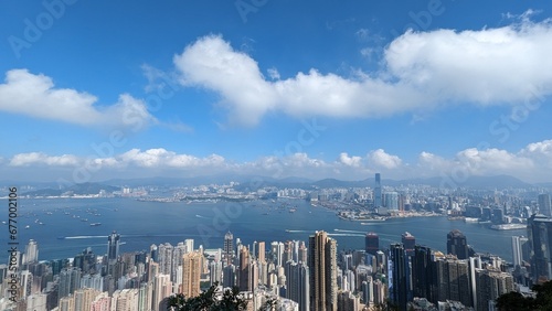 Panoramic Aerial View of Hong Kong Skyline and Victoria Harbour with Dense Skyscrapers, Boats, and Mountains on a Sunny Day with Blue Sky and Fluffy Clouds