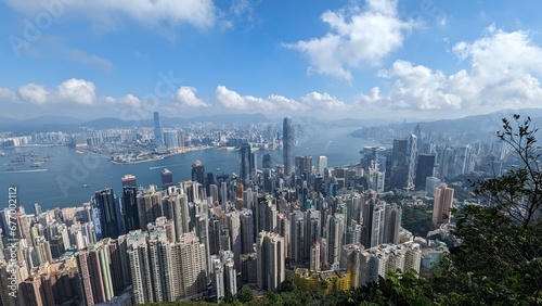 Panoramic Aerial View of Hong Kong Skyline and Victoria Harbour with Dense Skyscrapers  Boats  and Mountains on a Sunny Day with Blue Sky and Fluffy Clouds