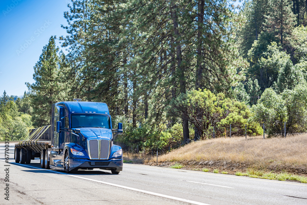 Bonnet powerful big rig semi truck tractor transporting fastened cargo on flat bed semi trailer driving on the multiline highway road Bonnet powerful big rig semi truck tractor transporting fastened cargo on flat bed semi trailer driving on the multiline highway road