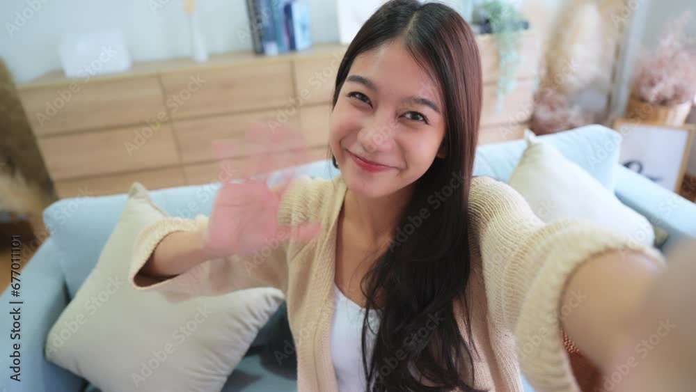 Pretty young asian female with big smile sitting at living room. She having fun taking light cheerful selfie on blurred background