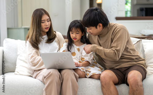 Father and mother with asian kid girl learn on laptop computer reviewing lesson study with online education e-learning.student look for educational knowledge in homeschool at home.Education