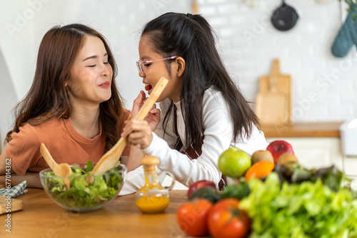 Portrait of enjoy happy love asian family mother and little asian girl daughter child having fun help cooking food healthy eat together with fresh vegetable salad and ingredient in kitchen.