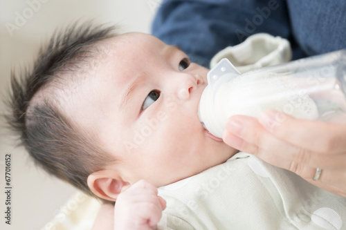 哺乳瓶でミルクを飲むベビー服姿の赤ちゃん ママを見ながら仰向けで顔にクローズアップ
