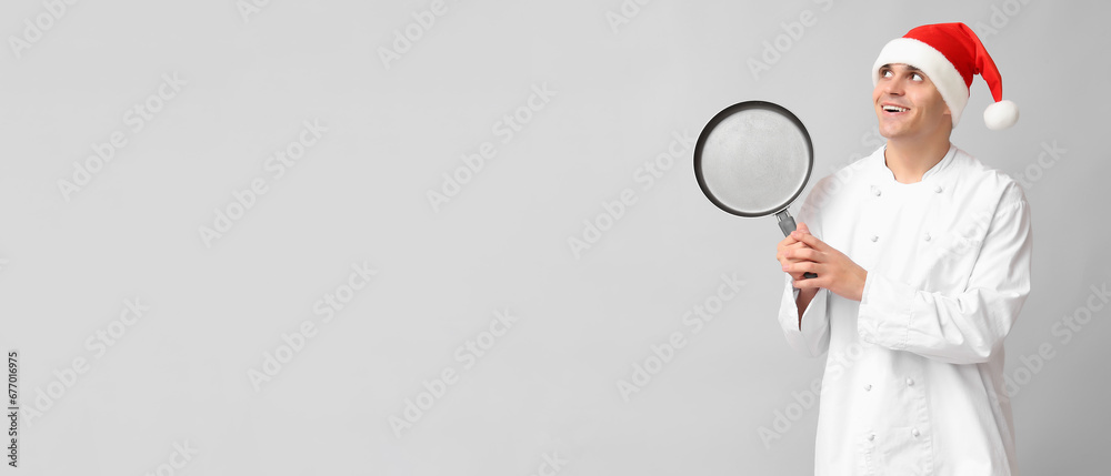 Male chef in Santa hat and with frying pan on grey background with space for text Male chef in Santa hat and with frying pan on grey background with space for text