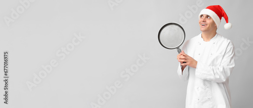Male chef in Santa hat and with frying pan on grey background with space for text © Pixel-Shot
