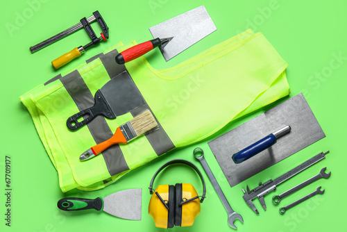 Set of construction tools and safety vest on green background