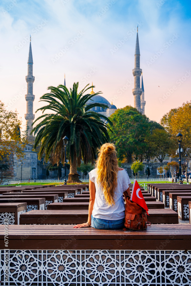 Fototapeta premium Woman tourist sitting on bench looking at the Blue mosque and palm tree, Istanbul, Turkey