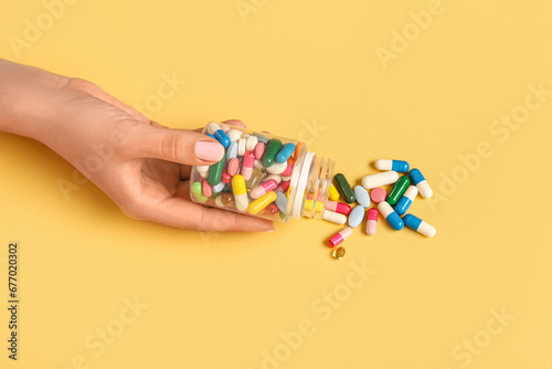 Woman holding jar with different pills on yellow background