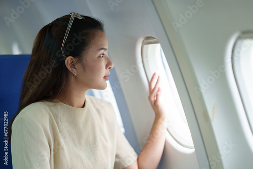 An Asian businesswoman or female entrepreneur on an airplane sits with the window open next to her business class seat to relax and view the scenery during her flight. Work lifestyle concept.