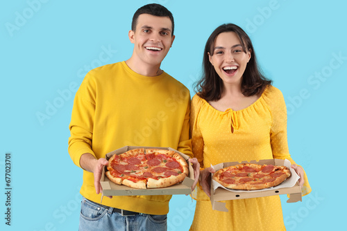 Young couple with tasty pepperoni pizza on blue background