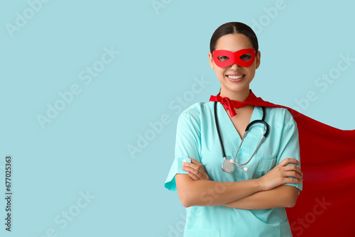 Young female doctor in superhero costume on blue background