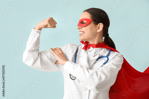 Beautiful female doctor in superhero costume showing muscles on blue background