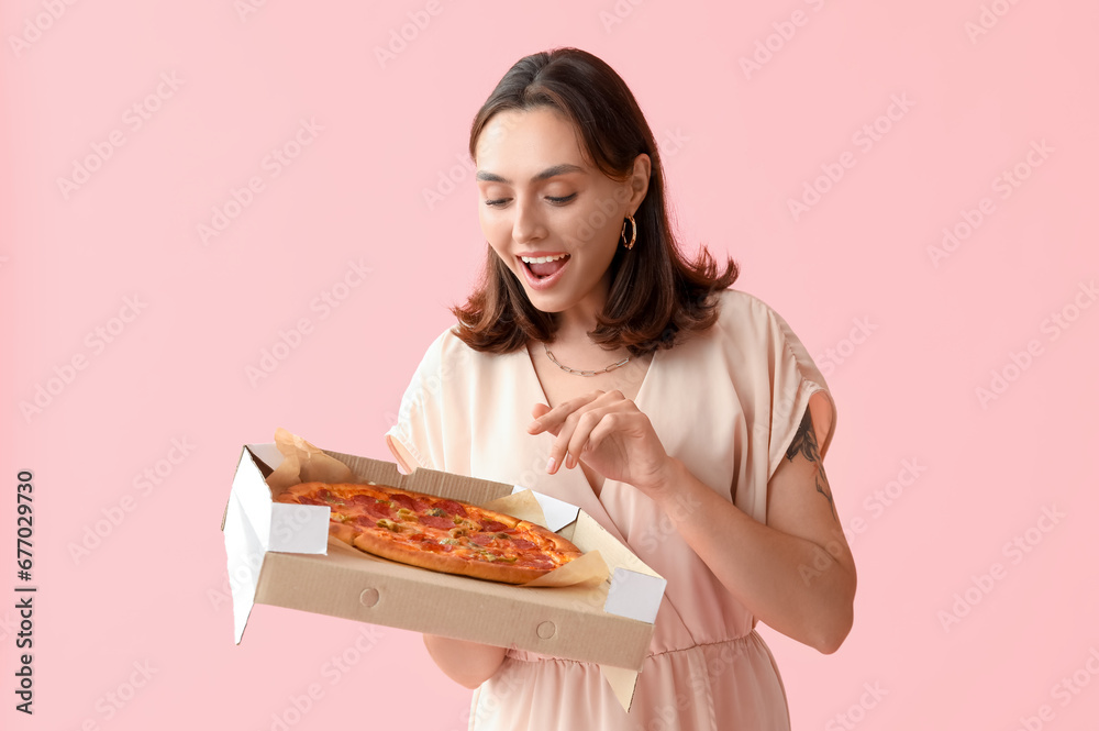 Young woman holding cardboard box with tasty pizza on pink background
