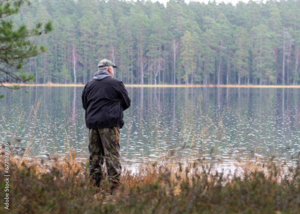 fisherman on the shore of a swamp lake, forest and swamp vegetation, rainy and cloudy day