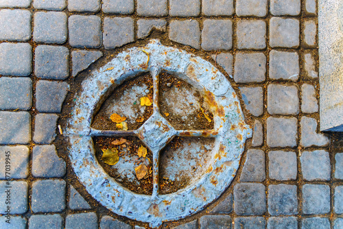 Very old manhole on the pavement made of square stones