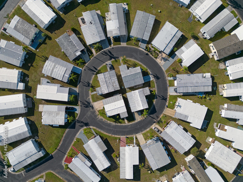 A mobile home neighborhood, configured in a circular layout, is shown from an aerial, daytime view among the community's streets.