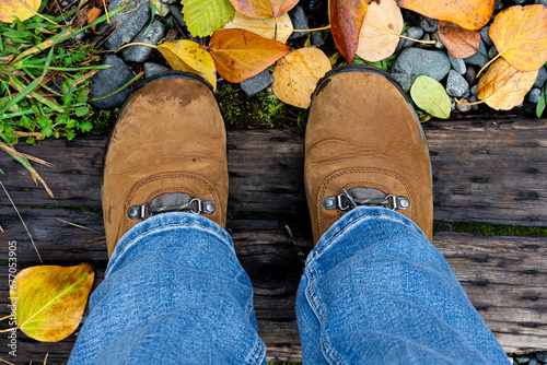 A top view image of a pair of tan hiking boots and an old railway timber with autumn colored leaves. 