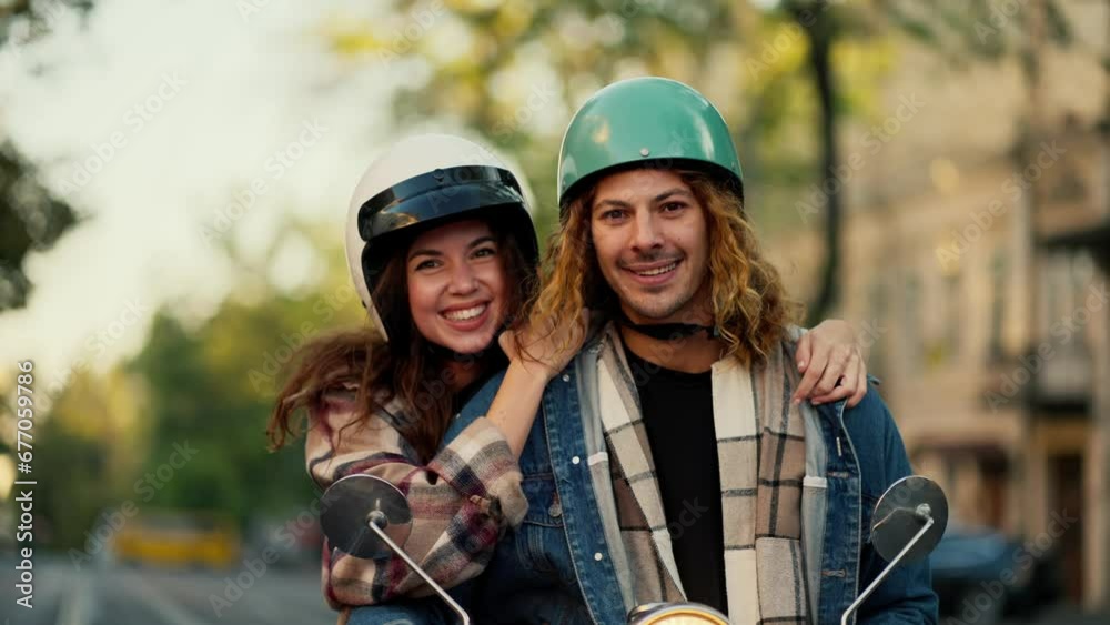 Portrait of a happy couple, a brunette girl in a plaid shirt hugs her boyfriend with long curly hair in a denim jacket and a green motorcycle helmet Near her motorcycle in the summer city Portrait of a happy couple, a brunette girl in a plaid shirt hugs her boyfriend with long curly hair in a denim jacket and a green motorcycle helmet Near her motorcycle in the summer city