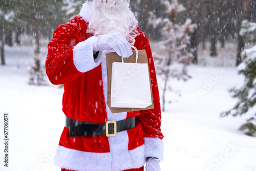 Santa Claus outdoor in winter and snow handing in hand eco paper bags with craft gift, food delivery. Shopping, packaging recycling, handmade, delivery for Christmas and New year