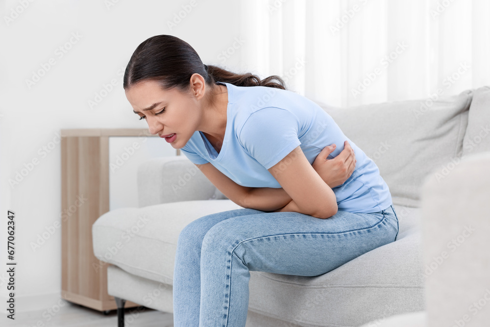 Woman suffering from abdominal pain on sofa at home. Unhealthy stomach Woman suffering from abdominal pain on sofa at home. Unhealthy stomach