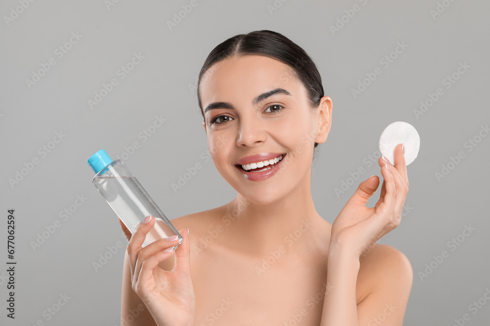 Beautiful woman holding makeup remover and cotton pad on light grey background Beautiful woman holding makeup remover and cotton pad on light grey background