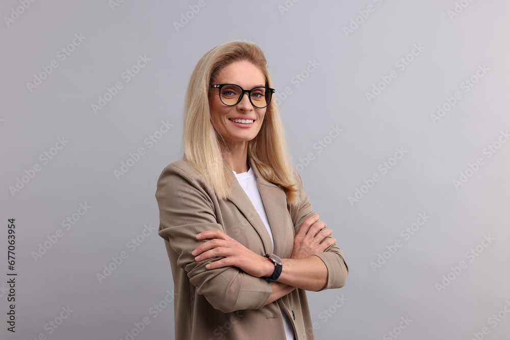 Portrait of smiling middle aged businesswoman with crossed arms on light grey background