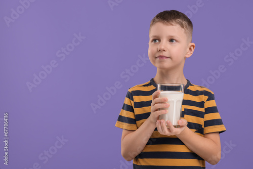 Cute boy with glass of fresh milk on violet background, space for text