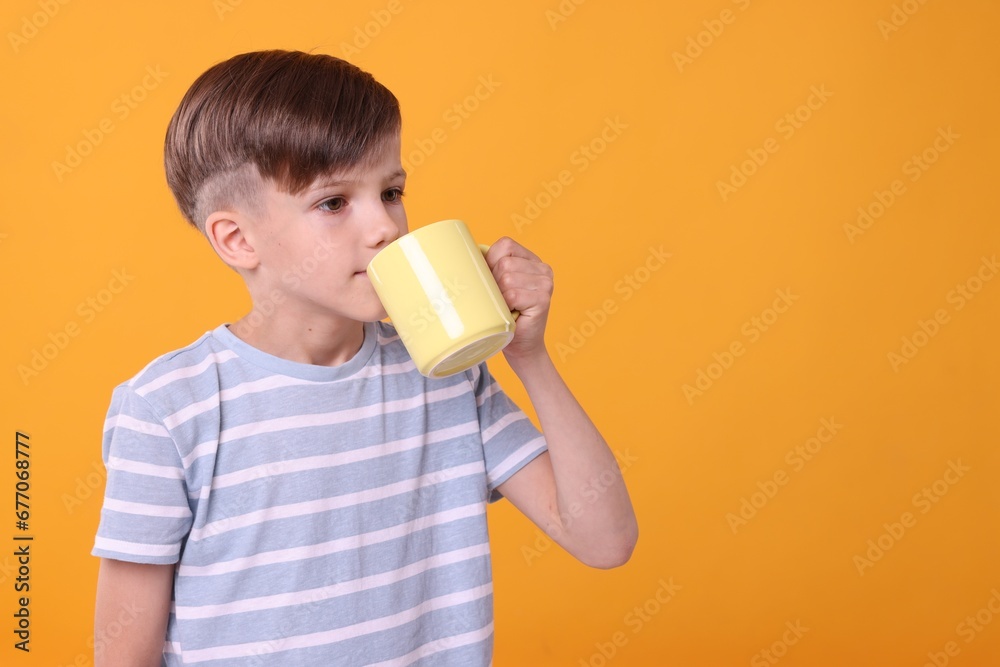 Cute boy drinking beverage from yellow ceramic mug on orange background, space for text Cute boy drinking beverage from yellow ceramic mug on orange background, space for text