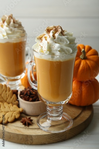 Tasty pumpkin latte with whipped cream in glasses, spices and cookies on white wooden table, closeup