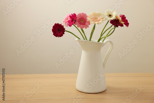 Jug with beautiful gerbera flowers on wooden table. Space for text