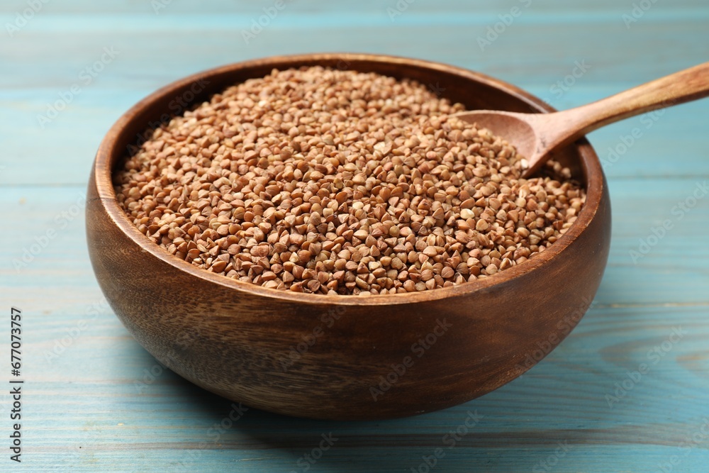 Bowl and spoon with dry buckwheat on light blue wooden table, closeup Bowl and spoon with dry buckwheat on light blue wooden table, closeup