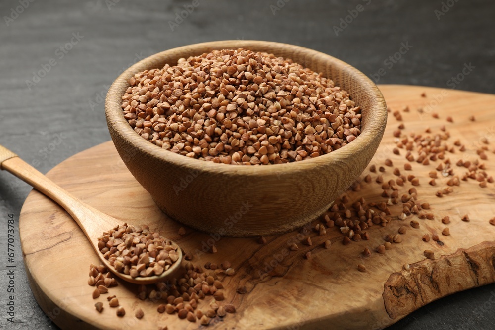 Bowl and spoon with dry buckwheat on black table, closeup Bowl and spoon with dry buckwheat on black table, closeup