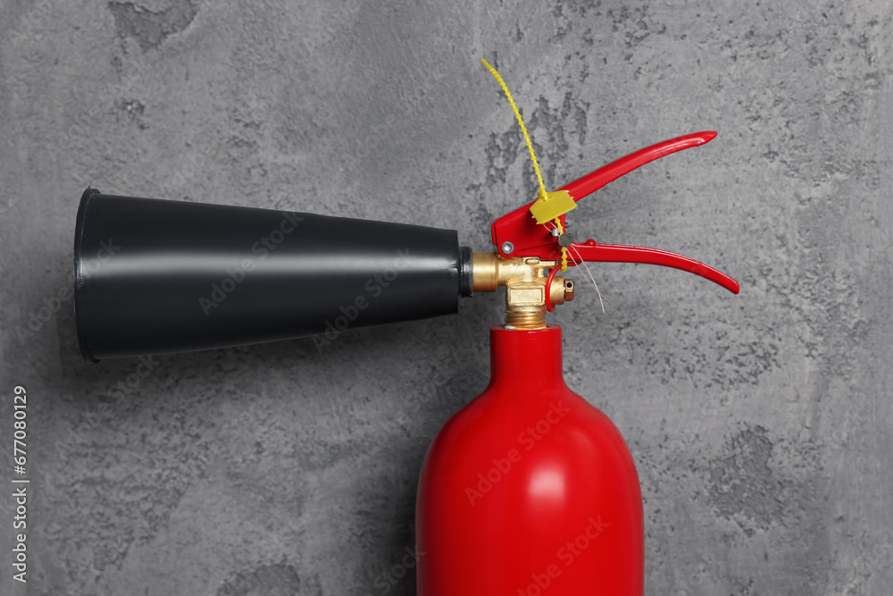 Naklejka premium Red fire extinguisher near grey wall, closeup