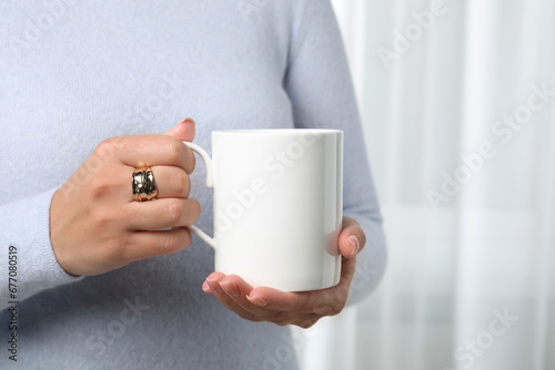 Woman holding white mug indoors, closeup. Mockup for design