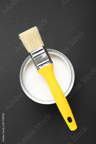 Can of white paint with brush on black background, top view