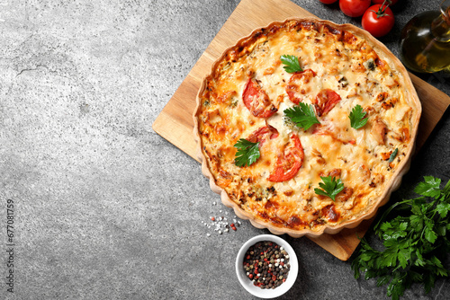 Tasty quiche with tomatoes  parsley and cheese served on grey textured table  flat lay. Space for text