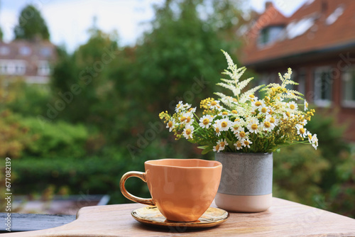 Cup of delicious chamomile tea and fresh flowers outdoors. Space for text