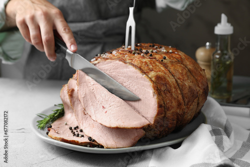 Woman cutting delicious baked ham at light grey table, closeup