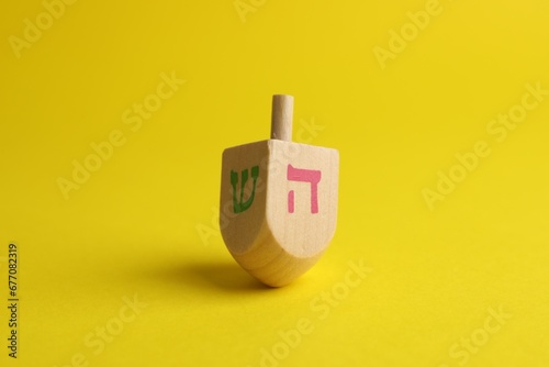 Wooden dreidel on yellow background. Traditional Hanukkah game